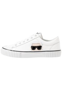 Weißer Leinenschuh mit runder Zehenpartie, Schnürdesign, Gummisohle und einem kleinen schwarzen und beige Sonnenbrillen-Patch an der Seite.
