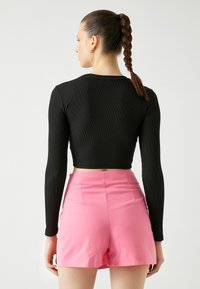Musta ribbed pitkähihaine crop-top, joka on yhdistetty korkeavyötäröisiin vaaleanpunaisiin shortsit. Topissa on tiukka muotoilu ja pyöreä kaula-aukko.