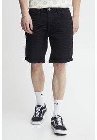 Sorte denimshorts med opsmøgede kant, med et standard fem-lomme design og metalknaplukning. Båret med sorte sneakers og hvide sokker.