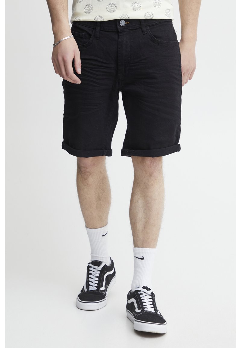 Sorte denimshorts med opsmøgede kant, med et standard fem-lomme design og metalknaplukning. Båret med sorte sneakers og hvide sokker.