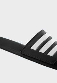 Black slide sandal with a textured strap featuring three white parallel stripes, a smooth sole, and gray stitching along the edges.