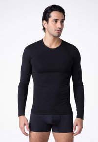 Maglietta nera a maniche lunghe, design attillato, collo a giro, texture liscia, indossata con pantaloni corti scuri e attillati, senza fantasie o accenti.