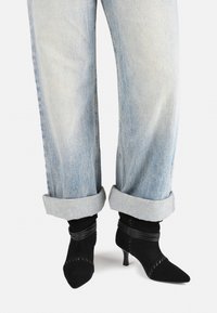 Mustad nahast ankle kingad terava ninaga ja õhukese kontsaga, kombineeritud kerge sinise denim jeaniga, millele on tehtud cuff. Kingad on varustatud tekstureeritud mustade ribadega.