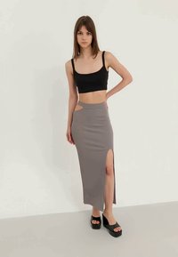 Jupe grise taille haute avec une fente sur le côté et un détail découpé, associée à un crop top noir. Le modèle porte des sandales compensées noires.