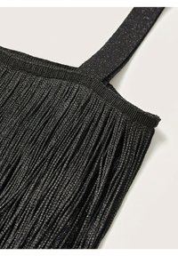 Gros plan sur un sac noir tissé avec de longues franges et une sangle en tissu scintillant sur un fond clair.