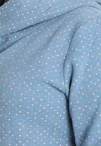 Tela azul con un patrón de pequeños lunares de colores, que presenta puntos en rosa claro, amarillo, verde y azul.