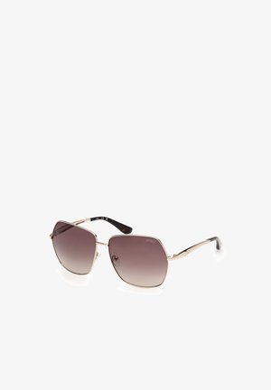 Gafas de sol con montura de metal dorado, lentes grandes y angulares con degradado marrón y puntas negras en las patillas, con la marca "GUESS" en la lente.