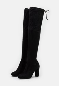 Botas negras de encima de la rodilla hechas de tela suave, con una textura lisa, punta afilada y tacón grueso, con lazos ajustables en la parte superior.