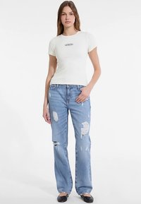 Bílé přiléhavé tričko s krátkými rukávy a černým logem. Kombinováno se světle modrými potrhanými džínami a černými balerínami.