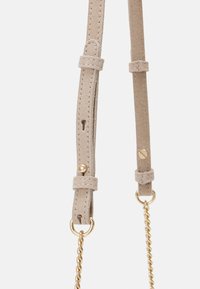 Beżowy zamszowy pasek na ramię z przeszywanymi detalami, posiadający złote akcesoria i akcent w postaci skręconego łańcucha. Regulowana długość i zapięcia.