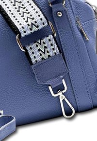 Blauwe leren handtas met textuur, voorzien van een afneembare schouderriem met een geometrisch zwart-wit patroon en zilveren hardware accenten.
