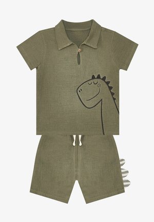 Set di polo verde oliva a maniche corte con grafica di un dinosauro, dettagli con bottoni e pantaloni corti coordinati con inserti a strisce sulla coda sul retro.