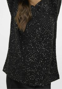 Zwart topje gemaakt van gestructureerde stof, versierd met talloze glanzende pailletten. Voorzien van een V-hals en losse mouwen.