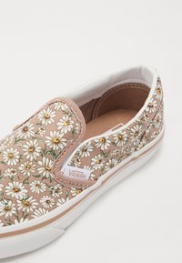 Vans slip-on sneakers i lys brun kanvas med hvitt tusenfryd mønster. Hvit gummisåle. Logomerke på siden.