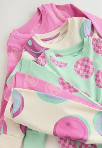 Neljä crewneck-neuletta taiteltuna yhteen: vaaleanpunainen, mintunvihreä ja kermaisen värinen kangas, jossa on pyöreitä kuvioita, esittäen hymyileviä naamioita ja ruudullisia kuvioita.