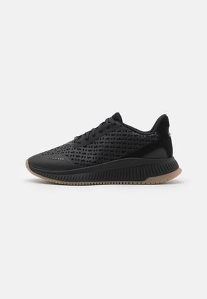 Black athletic shoes with a perforated upper, textured surfaces, rubber sole, and contrasting tan outsole. Lace-up design with minimal branding.