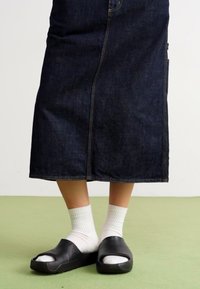 Mustad mustad sussid valgete sokkidega, koos pika tumeda denimseelikuga. Seelikul on eesmine õmblus ja sirge lõike disain.