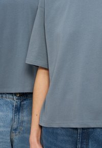 Δύο άτομα που φορούν άνετες ανοιχτό μπλε μπλούζες και μπλε τζιν στέκονται κοντά το ένα στο άλλο, δείχνοντας το μέσο μέρος και τα χέρια τους.