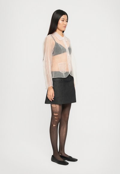 Kumerõhuga läbipaistev pikkade varrukatega pluus, kombineeritud musta denimpidža ja purustatud mustade sukkpükste ning lame mustade kingadega.