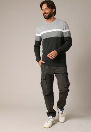 Pull rayé gris et noir avec un col rond, associé à un pantalon cargo sombre et des baskets blanches. Tenue décontractée avec une coupe ample.
