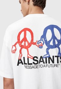 Camiseta blanca con personajes de signo de paz en rojo y azul sosteniendo manos sobre el texto "ALLSAINTS" y "MENSAJE A UN FUTURO" en la parte posterior.