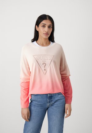 Maglione in gradiente rosa con logo a triangolo di Guess e un punto interrogativo, maniche lunghe e texture morbida, abbinato a jeans blu di denim.