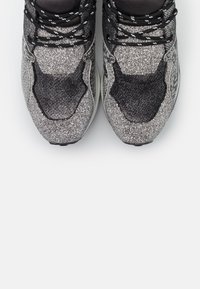 Baskets de sport noires et argentées avec une tige texturée et une finition réfléchissante, un col rembourré et un design de lacets contrastants.