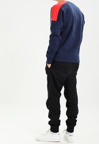 Marinblå sweatshirt med röd axelaccent, i kombination med svarta joggers och vita sneakers. Har en avslappnad passform och ribbade muddärmar.