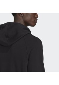 Felpa nera con cappuccio caratterizzata da una texture morbida, con cappuccio regolabile e una vestibilità comoda, che mostra una superficie liscia e dettagli di cucitura minimi.