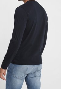Marineblaues Langarm-T-Shirt aus glattem Stoff, mit Rundhalsausschnitt und taillierter Form, kombiniert mit hellblauen Denim-Jeans.