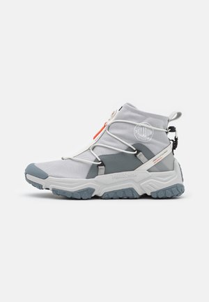 Sneaker Palladium grigia e bianca alta con suola robusta, lacci elastici e linguetta, progettata per prestazioni urbane e impermeabili.