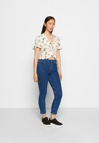 Top floral com mangas curtas em creme, combinado com jeans skinny de cintura alta azuis e ténis pretos com sola branca.