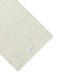 Tessuto intrecciato grigio chiaro con una superficie texturizzata, caratterizzato da una piccola etichetta bianca con le lettere "AX" ricamate in filo argentato.