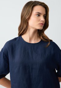 Top in lino blu navy con scollo rotondo e maniche corte. Il tessuto ha una finitura leggermente strutturata e una vestibilità morbida.