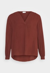 Blouse couleur rouille avec un décolleté en V, des manches longues et un ourlet incurvé. Fabriquée dans un tissu doux avec un léger drapé au niveau des épaules.