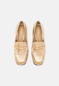 Mocassins en cuir doré avec une finition texturée, présentant un bout mocassin détaillé en surpiqûre et une semelle plate pour un look moderne.