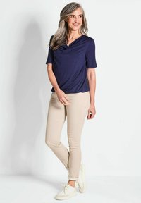 Marineblaues Kurzarmoberteil mit Drapierung am Ausschnitt, kombiniert mit hellbeigen Slim-Fit-Hosen und cremefarbenen Sneakern mit aufgerollten Ärmeln.