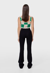 Gebreide tanktop met groen en beige ruitpatroon, gecombineerd met aansluitende zwarte geribbelde flared broeken. Soepele textuur, blootstelling van de buik.