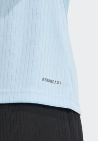 Lichtblauw geribbeld sporttop met een logo op de zoom, gecombineerd met zwarte gestructureerde onderstukken. De stof lijkt zacht en ademend te zijn.