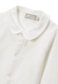 Chemise à col blanc en tissu doux, avec une patte de boutonnage et une finition texturée. Étiquette de la marque visible à l'intérieur du col.