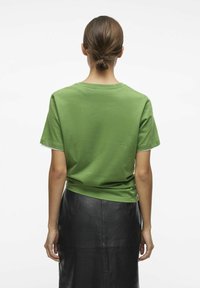 Camiseta de algodón verde de manga corta, con escote de cuello redondo y un ajuste relajado, combinada con una falda de cuero negra con un acabado texturizado.