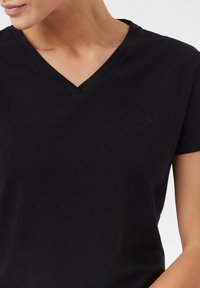 Zwarte v-hals t-shirt van zachte stof, met een subtiele reliëf tijgerkoplogo op de linkerkant van de borst, korte mouwen.