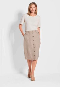 Beige Leinenrock mit Knopfleiste, zwei Seitentaschen und einem elastischen Bund. Kombiniert mit einem hellen, strukturierten Oberteil und Wedgesandalen.
