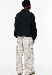Black jacket with a brown collar, loose-fitting light cargo pants with a textured white and gray pattern, featuring side pockets and a relaxed shape.