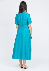 Türkises Kleid mit kurzen Ärmeln, knielang, mit taillierter Passform und dekorativen Nähten. Glatte, leichte Stoffqualität.