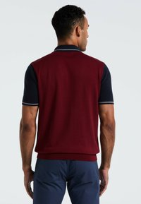 Gebreide polovest in bordeaux met marineblauwe korte mouwen. Kenmerken zijn een geribde kraag en zoom, een soepele textuur en contrasterende afwerking op de mouwen.