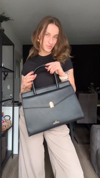 Schwarze Ledertasche mit strukturiertem Design, oberen Tragegriffen, goldenen Hardware-Details und einem Klappenverschluss. Glatte Textur mit einem minimalistischen Look.