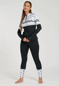Top sportivo nero con una sezione bianca a motivo che presenta fiocchi di neve e zigzag, abbinato a leggings neri accentuati da dettagli bianchi ai polsini.