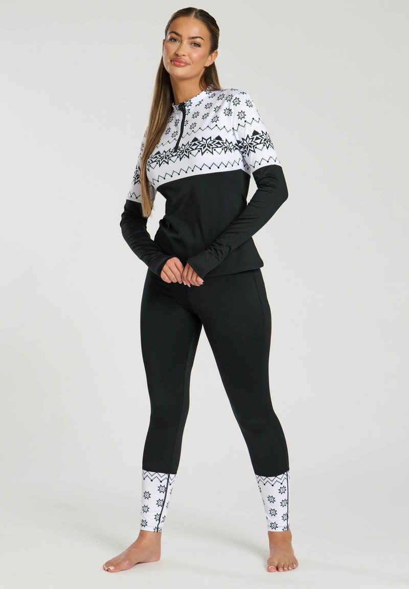 Top sportivo nero con una sezione bianca a motivo che presenta fiocchi di neve e zigzag, abbinato a leggings neri accentuati da dettagli bianchi ai polsini.