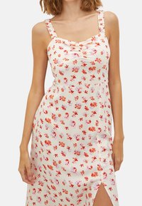Blumenkleid mit einem hellen Creme-Hintergrund, verziert mit roten und rosa Blumen, quadratischem Ausschnitt und gerafften Trägern, mit einem Seitenschlitz.